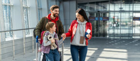 A New Zealand family with school-aged child arriving home at the airport with luggage, warm summer light through the windows suggesting the start of a new school year.