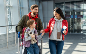 A New Zealand family with school-aged child arriving home at the airport with luggage, warm summer light through the windows suggesting the start of a new school year.